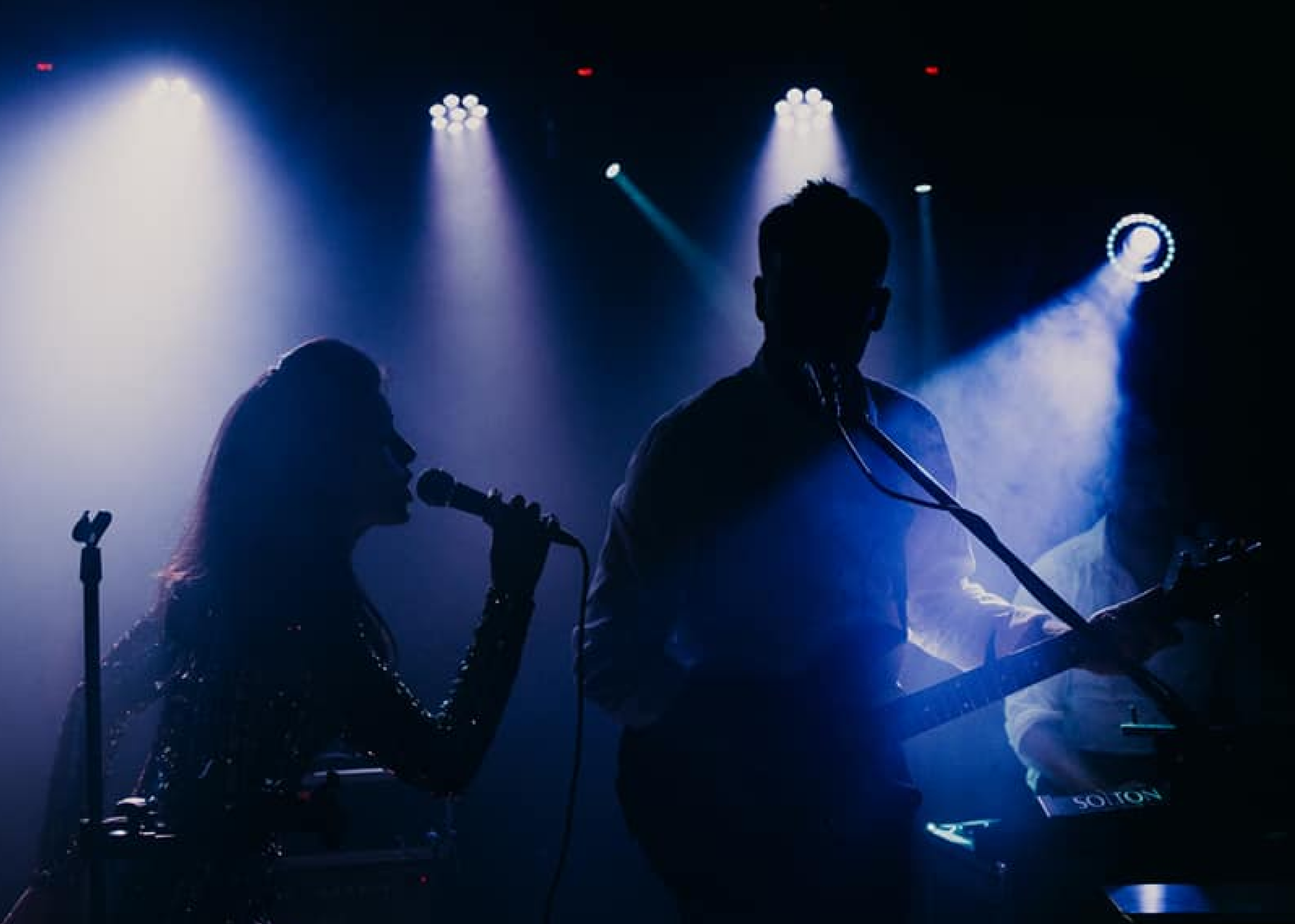 Zespół muzyki rozrywkowej Ostrowscy Band, wokalistka śpiewająca na scenie do mikrofonu i osoba grająca na gitarze, koncert w ciemności, efekty specjalne - światła na scenie.